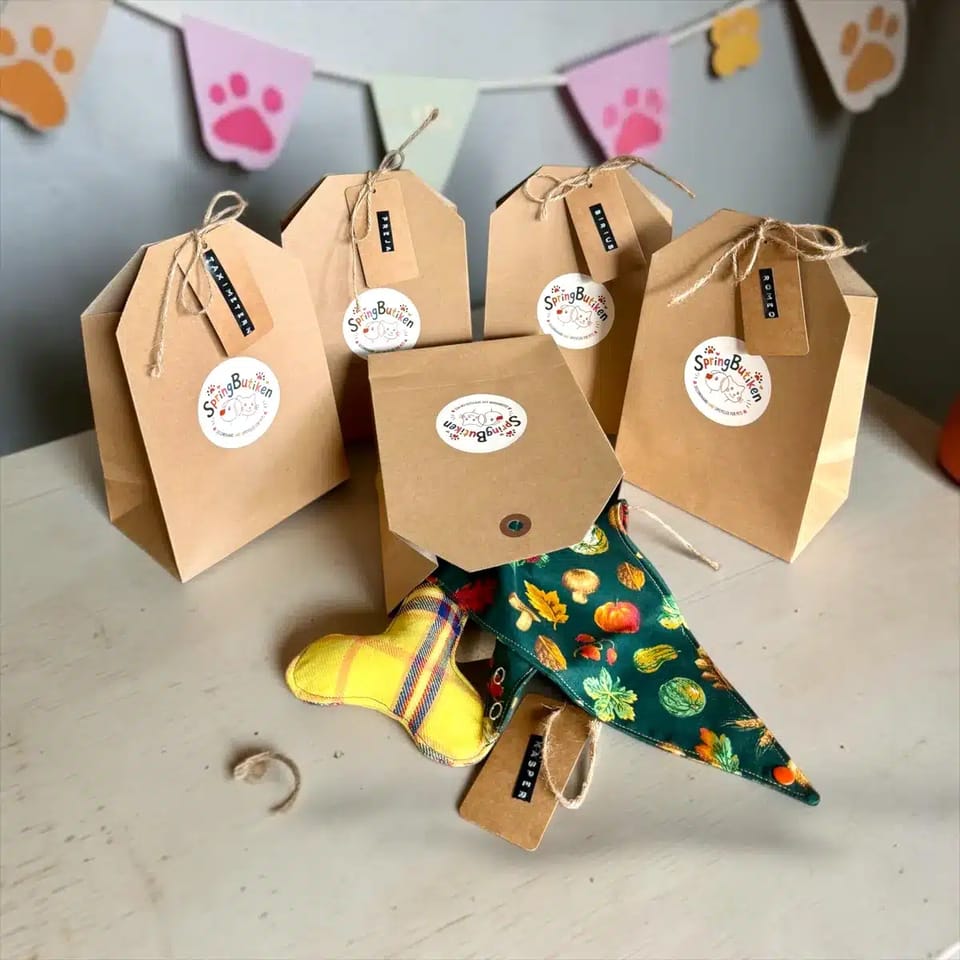 Presentförpackningar i kraftpapper med hundarnas namn på etiketterna, bredvid en bandana och en leksak
