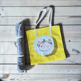 Gul väska med ljusblå handtag och SpringButiken-logotyp, bredvid en hopvikt blå vattentät matta.