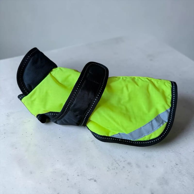 Reflektor detalj Hundjacka: a lime-green dog jacket with dark edging and a reflective strip.